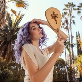 Woman with purple colored hair holding a mirror