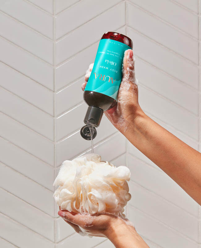 Hand squeezing AURA Body Wash onto a loofa